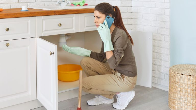 Woman dealing with a leak under the sink before emergency plumber arrives.