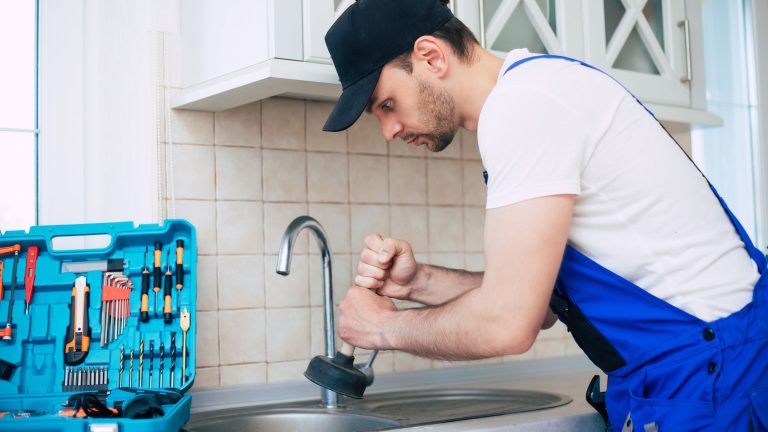 Plumber using a plunger to fix a kitchen sink while explaining what block drains in homes