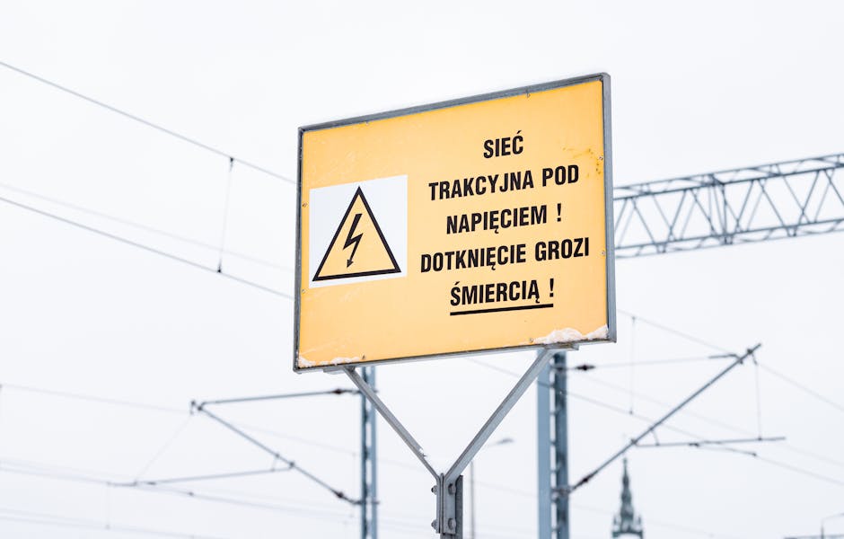 Yellow warning sign in Polish with electric symbol, cautioning about high voltage on railway lines.