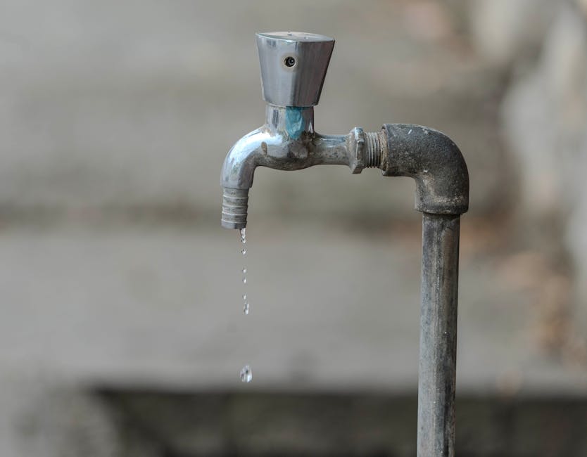 Close-up image of an outdoor water tap with a single droplet falling, highlighting water conservation.