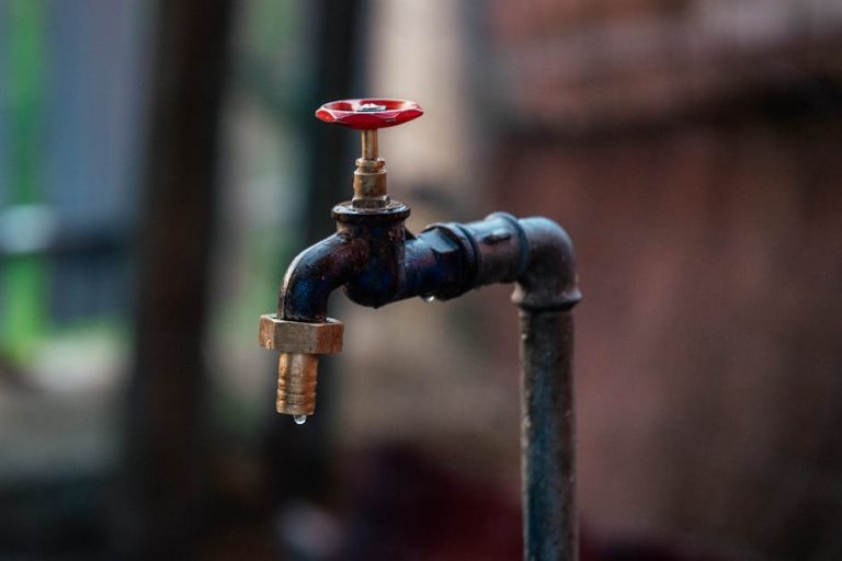 Close-up of a rusty outdoor water faucet with a single droplet falling from the spout.