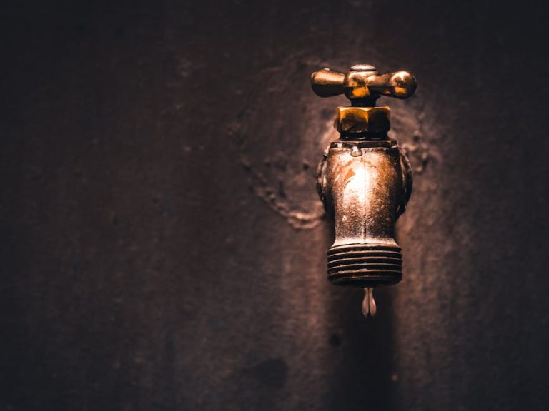 A close-up view of a vintage brass faucet with a single water droplet against a dark background.