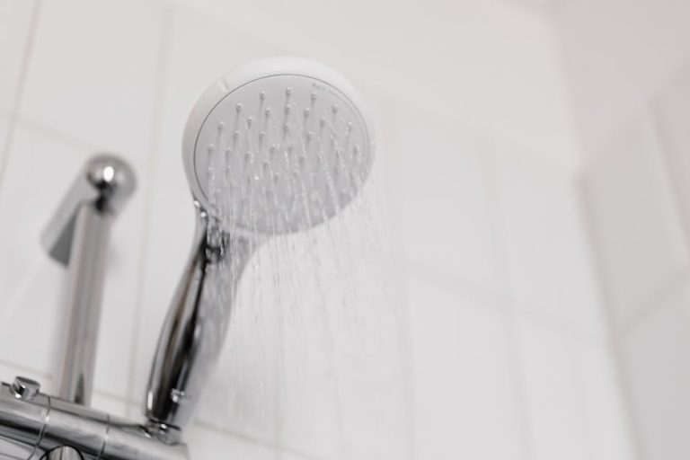 Stylish clean shower head with water flow in a white tiled bathroom.