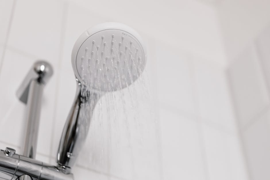 Stylish clean shower head with water flow in a white tiled bathroom.